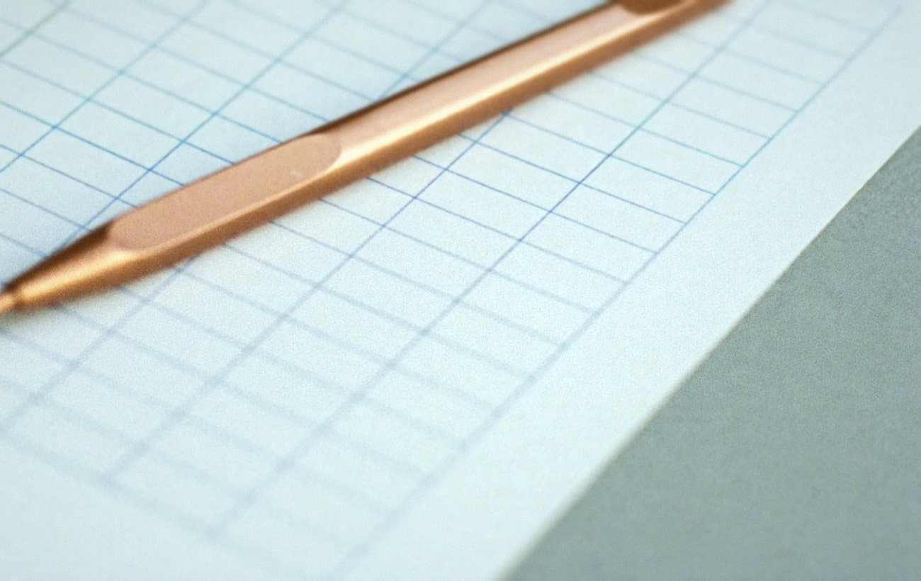 Ruled ledger paper with a copper coloured pen resting across its columns.